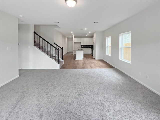 unfurnished living room featuring recessed lighting, stairway, baseboards, and light carpet