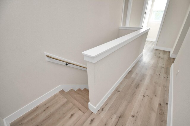 corridor featuring baseboards, an upstairs landing, and light wood-style flooring