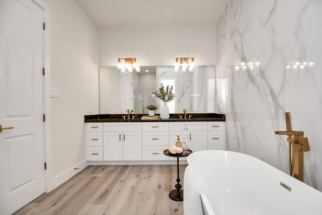 bathroom with a freestanding bath, double vanity, wood finished floors, and a sink