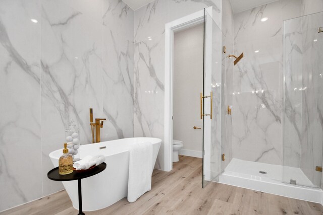 bathroom with toilet, a freestanding tub, wood finished floors, and a marble finish shower