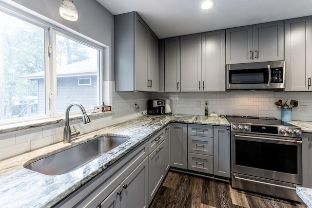 kitchen featuring decorative backsplash, a sink, gray cabinetry, dark wood-style floors, and stainless steel appliances