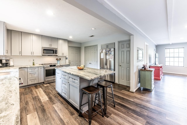 kitchen featuring gray cabinets, dark wood-style flooring, appliances with stainless steel finishes, and a kitchen breakfast bar