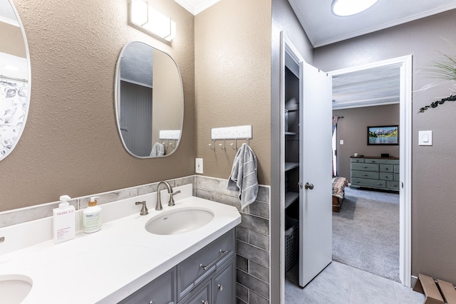 full bathroom featuring a textured wall, a sink, double vanity, tile patterned floors, and ornamental molding