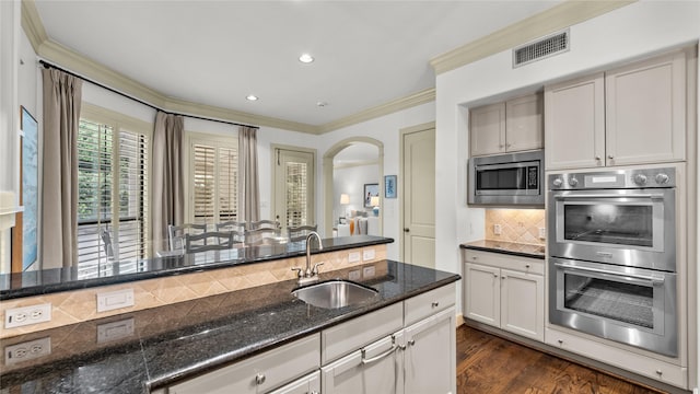 kitchen featuring dark stone counters, a sink, arched walkways, appliances with stainless steel finishes, and visible vents