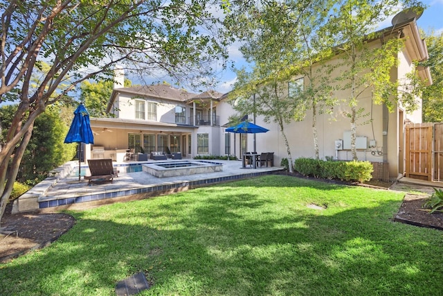 back of property with a lawn, a patio, an in ground hot tub, and stucco siding