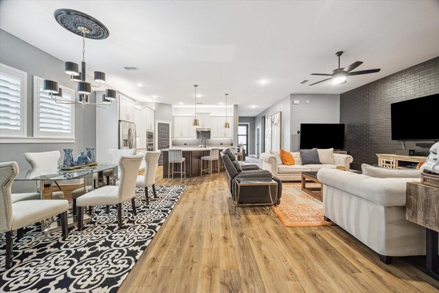 living room with recessed lighting, visible vents, light wood-style floors, brick wall, and ceiling fan with notable chandelier