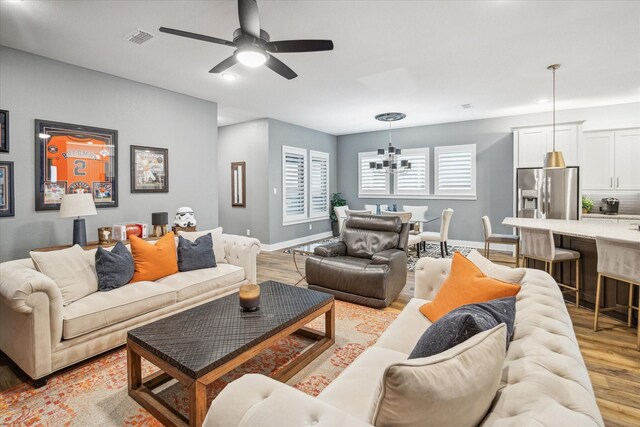 living room with visible vents, light wood finished floors, baseboards, and ceiling fan with notable chandelier