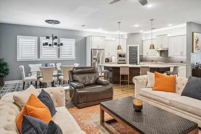 living room featuring recessed lighting, light wood-style flooring, and ceiling fan with notable chandelier
