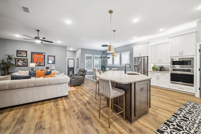 kitchen featuring stainless steel appliances, a kitchen breakfast bar, a sink, light wood-type flooring, and open floor plan