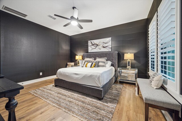 bedroom with wood finished floors, visible vents, and an accent wall