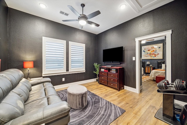 living room featuring a ceiling fan, baseboards, a textured wall, and light wood-type flooring