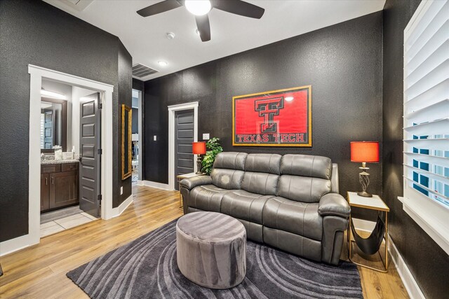 living room with light wood finished floors, baseboards, visible vents, ceiling fan, and a textured wall