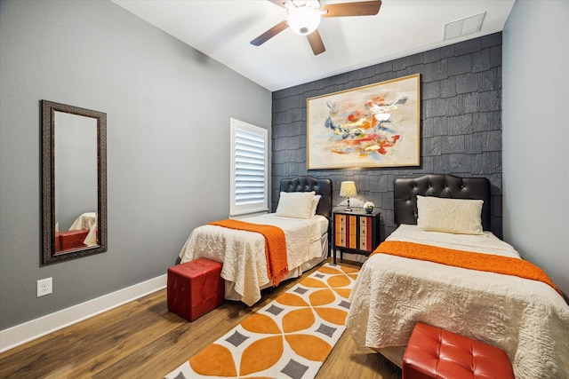bedroom with an accent wall, wood finished floors, ceiling fan, baseboards, and visible vents