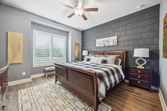 bedroom with ceiling fan, baseboards, an accent wall, and wood finished floors