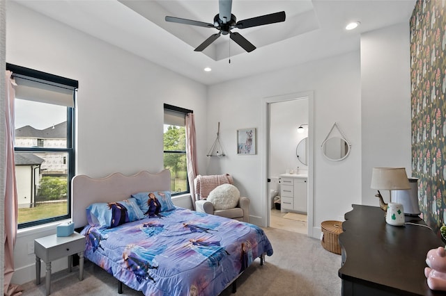 bedroom featuring recessed lighting, a tray ceiling, light carpet, ceiling fan, and ensuite bathroom