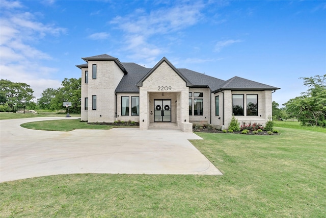 french country inspired facade with brick siding, roof with shingles, and a front yard