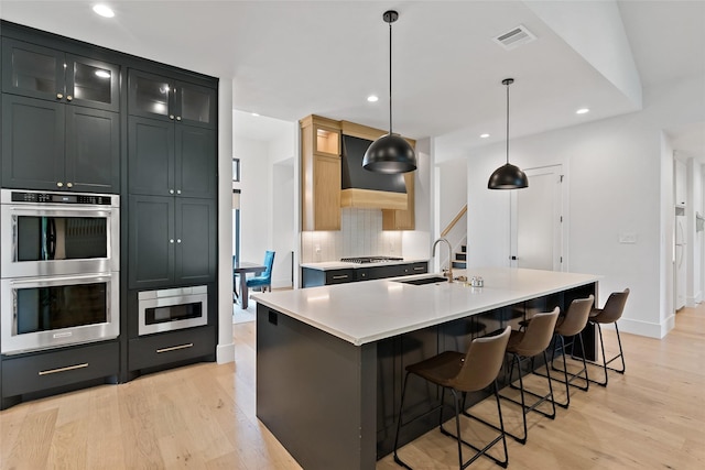 kitchen with backsplash, appliances with stainless steel finishes, a sink, and light wood-style floors