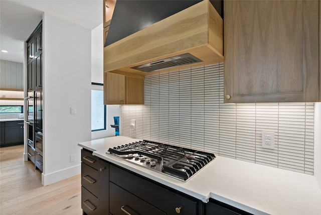 kitchen with stainless steel gas stovetop, light countertops, light wood-style flooring, custom range hood, and baseboards