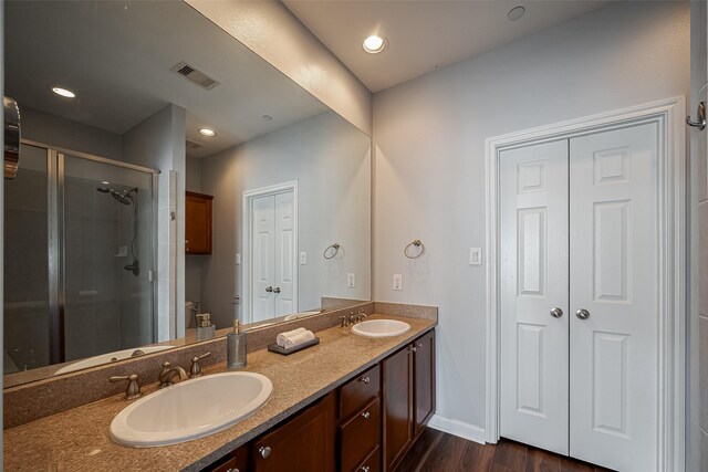 full bath featuring double vanity, wood finished floors, visible vents, a sink, and a stall shower