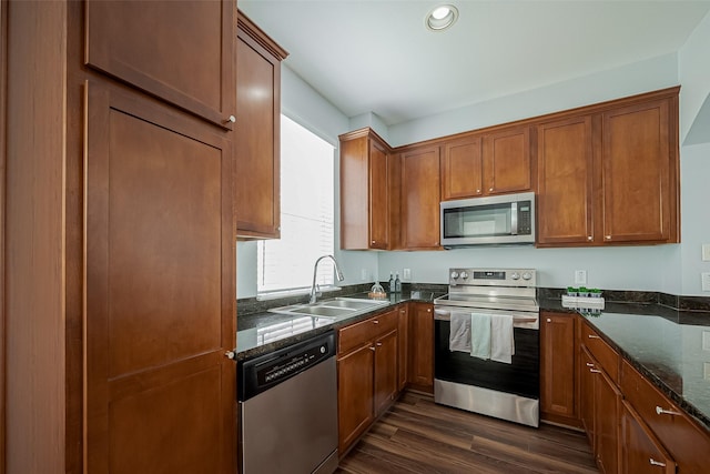 kitchen with stainless steel appliances, a sink, dark stone countertops, dark wood finished floors, and brown cabinetry