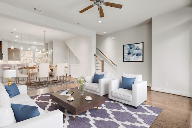 living area with stairway, visible vents, light wood-style floors, baseboards, and ceiling fan with notable chandelier