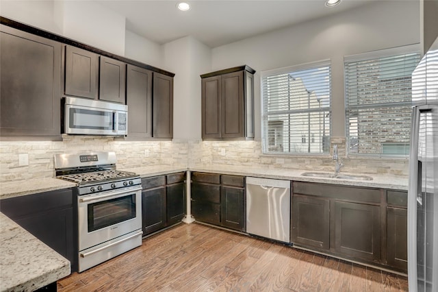 kitchen with backsplash, light stone countertops, stainless steel appliances, and a sink
