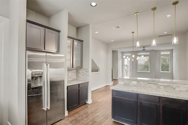 kitchen with light stone counters, backsplash, visible vents, light wood-type flooring, and stainless steel fridge
