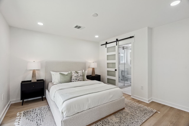 bedroom featuring a barn door, wood finished floors, baseboards, visible vents, and recessed lighting