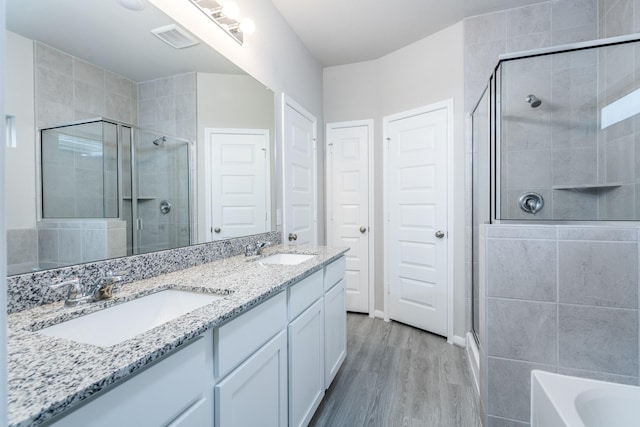 bathroom featuring a sink, double vanity, a shower stall, and wood finished floors