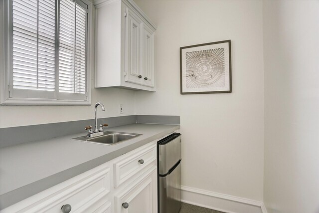 kitchen with white cabinets, freestanding refrigerator, light countertops, and a sink