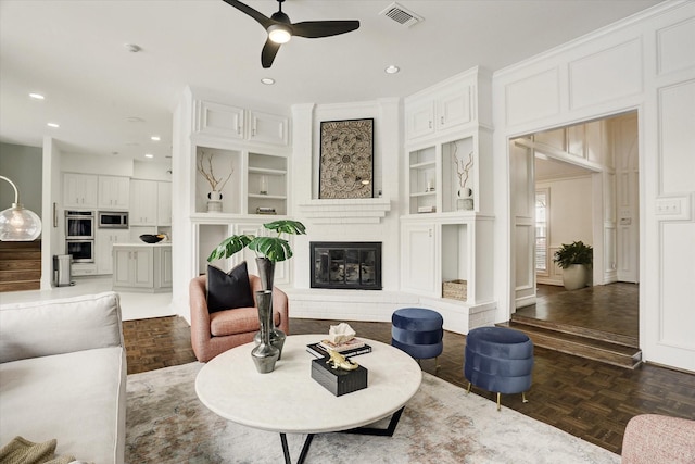 living room with recessed lighting, visible vents, a glass covered fireplace, built in shelves, and ceiling fan