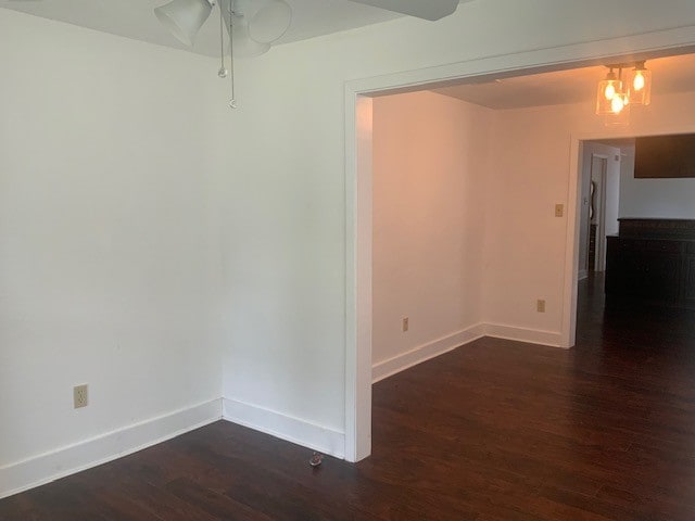 empty room featuring a ceiling fan, baseboards, and dark wood-type flooring