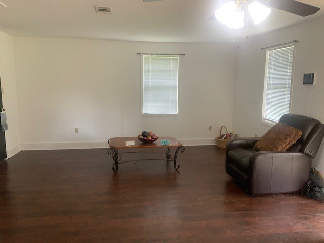 unfurnished living room featuring ceiling fan, baseboards, wood finished floors, and visible vents
