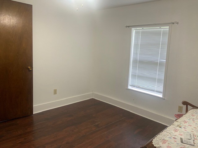 unfurnished bedroom featuring baseboards and dark wood-style flooring