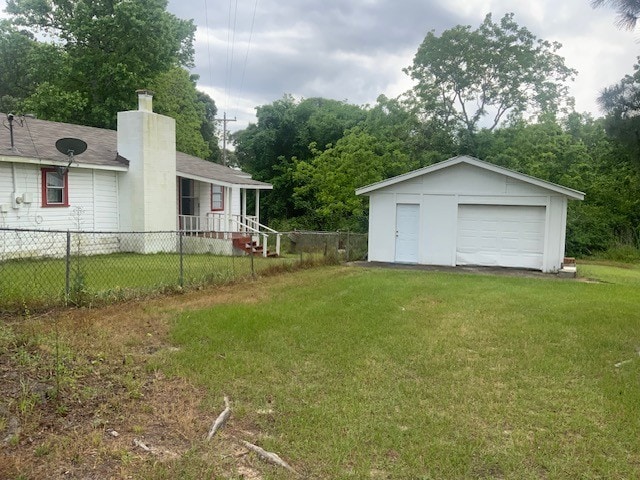 view of yard featuring a detached garage, an outbuilding, fence, and driveway