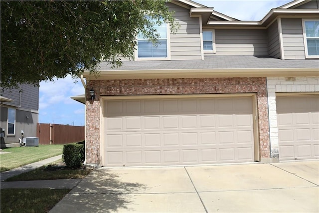 garage with central AC unit, concrete driveway, and fence