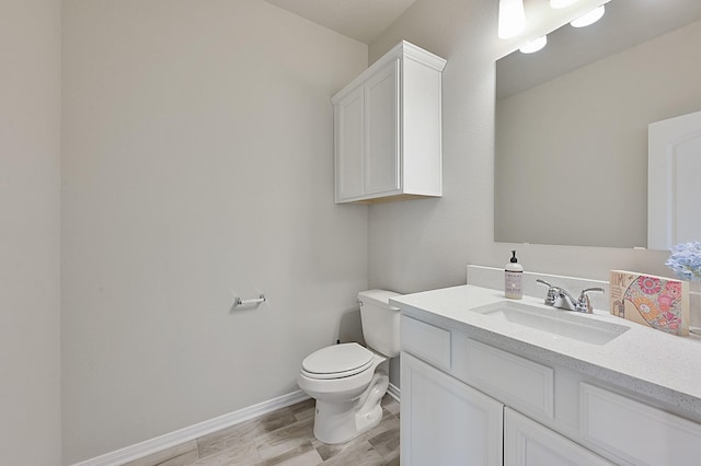 half bath featuring baseboards, wood finished floors, vanity, and toilet