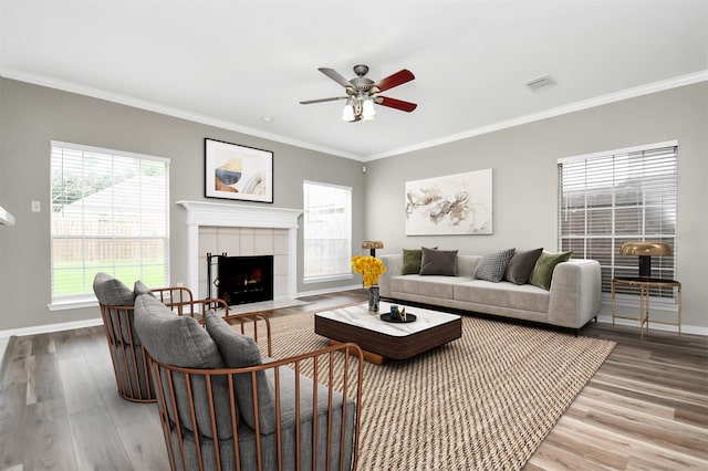 living room with wood finished floors, a ceiling fan, ornamental molding, baseboards, and a fireplace