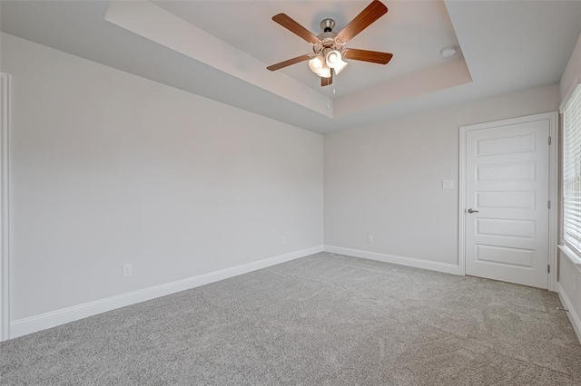 unfurnished room featuring ceiling fan, carpet floors, a tray ceiling, and baseboards