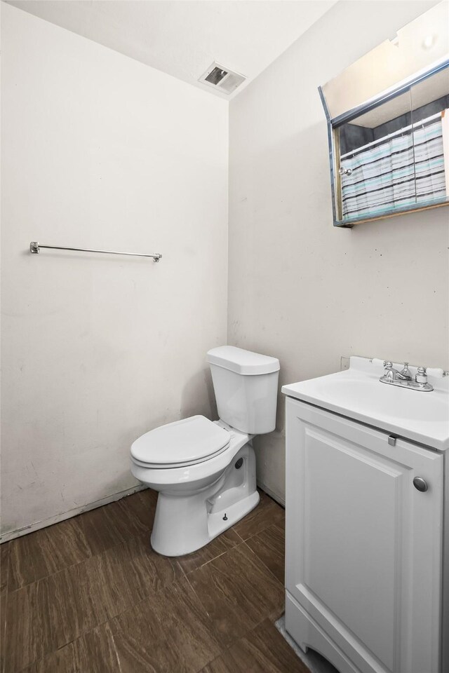 half bath with toilet, vanity, and visible vents