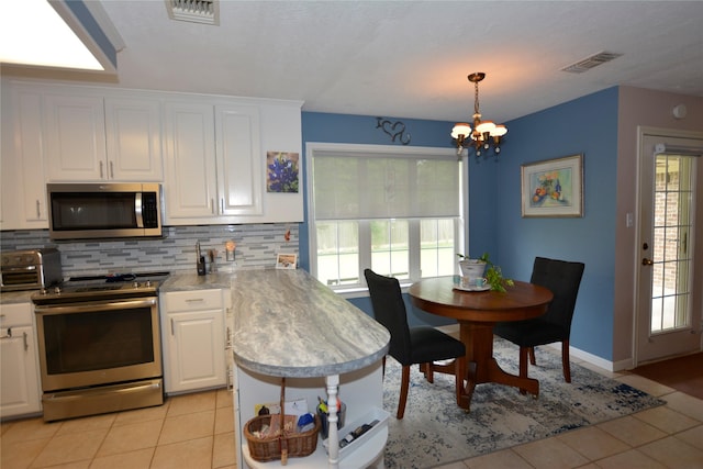 kitchen with light tile patterned floors, an inviting chandelier, white cabinets, and appliances with stainless steel finishes