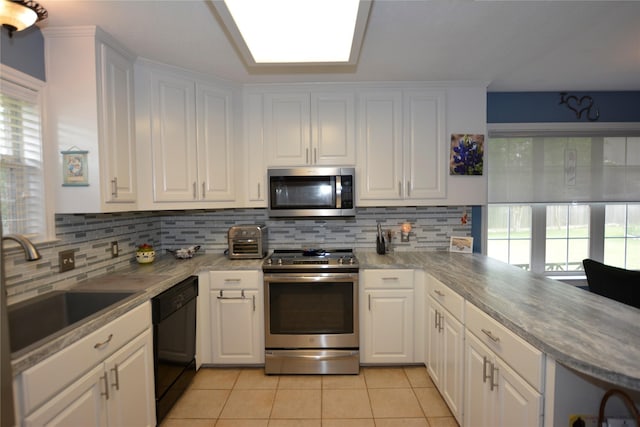 kitchen with light tile patterned floors, tasteful backsplash, white cabinets, a sink, and stainless steel appliances
