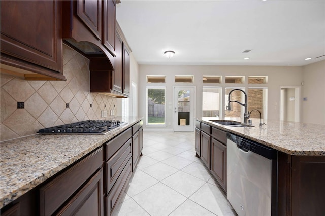 kitchen with appliances with stainless steel finishes, tasteful backsplash, a center island with sink, a sink, and light stone counters