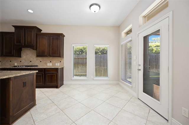 kitchen featuring dark brown cabinets, light stone counters, plenty of natural light, decorative backsplash, and light tile patterned floors