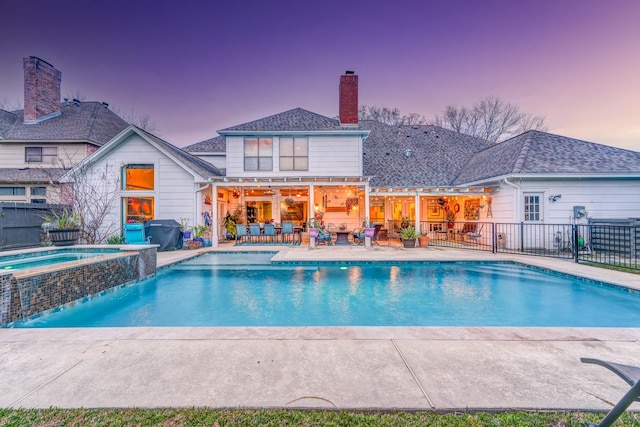 pool at dusk with fence, outdoor lounge area, a pool with connected hot tub, and a patio
