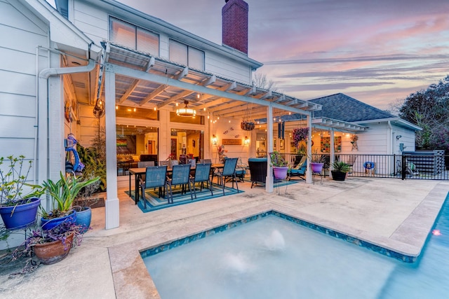 back of property at dusk with a pergola, a patio area, a chimney, outdoor dining area, and a fenced in pool