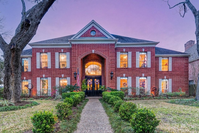 colonial-style house with brick siding, french doors, and a front lawn