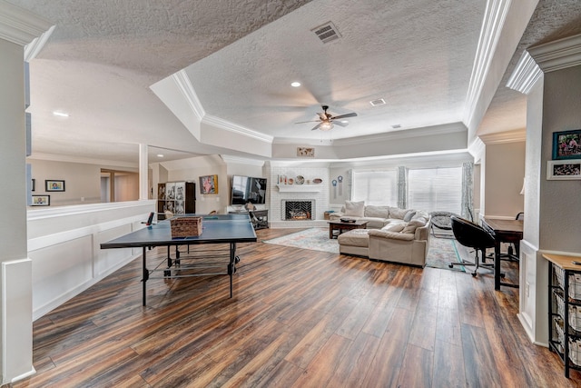 living area featuring ceiling fan, visible vents, crown molding, a fireplace, and dark wood-style flooring