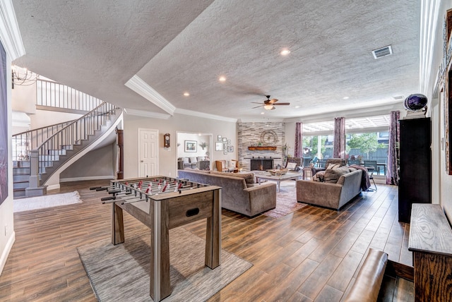 recreation room featuring a ceiling fan, wood finished floors, a textured ceiling, a fireplace, and visible vents