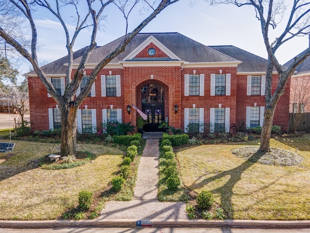 view of front of house with brick siding, french doors, roof with shingles, and a front yard